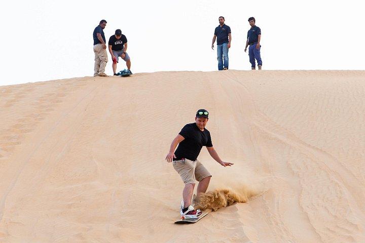 Les voyageurs montent des planches de sable sur les dunes près de Dubaï.